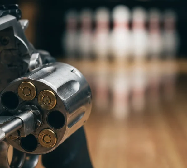 Gros plan sur le barillet d'un revolver .357 Magnum avec des balles visibles et une quille de bowling floue en arrière-plan