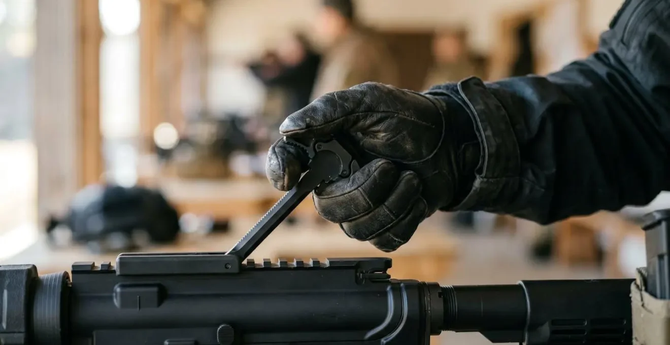 Gros plan sur une main gantée actionnant un levier d'armement élargi sur une carabine, montrant la prise sécurisée